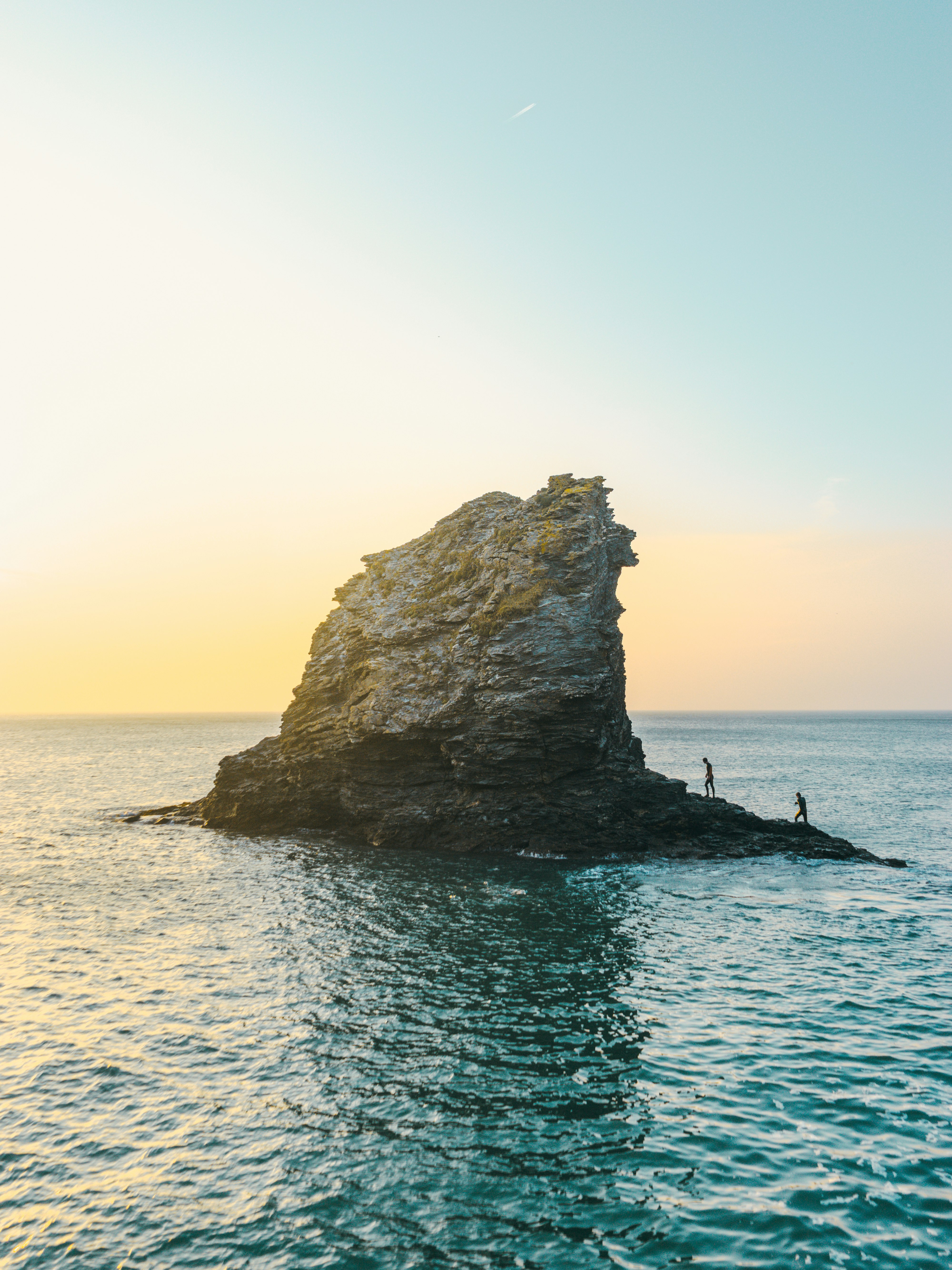 two people standing on rock formation surrounded by body of water during golden hour